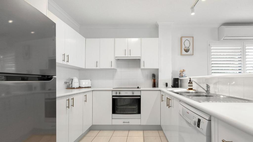 a white kitchen with white cabinets and a sink at Unit 3 21 Park Generous and Comfortable Beachside Abode in Sunshine Beach