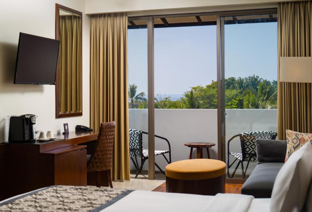 a hotel room with a bed and a desk and a balcony at MERUSAKA Nusa Dua in Nusa Dua
