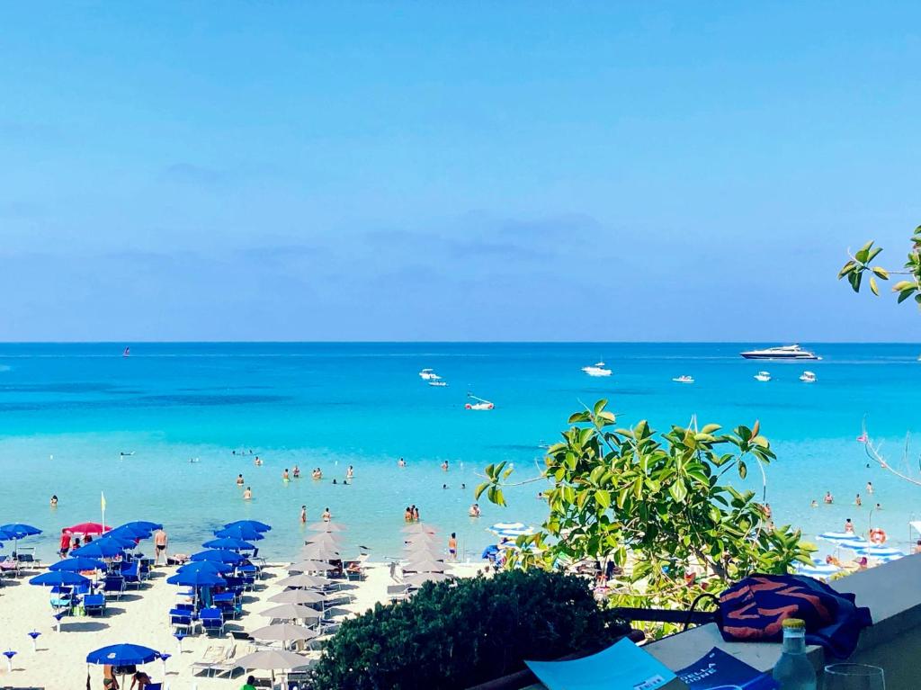 a beach with blue umbrellas and people in the water at Hotel Capo San Vito by Geocharme in San Vito lo Capo