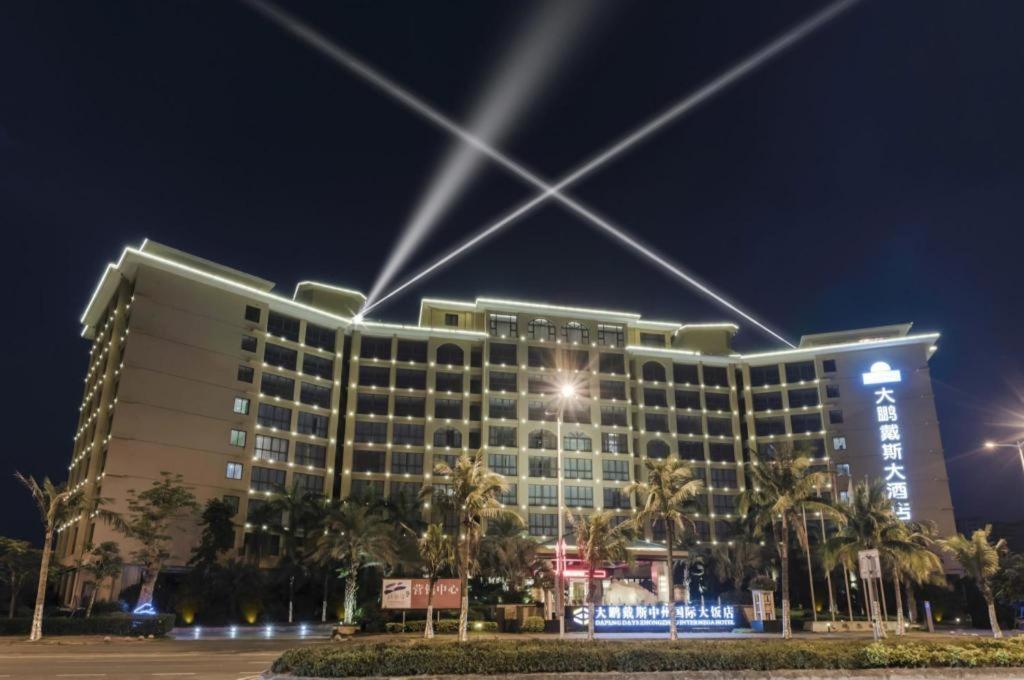 ein Hotel in der Nacht mit Palmen davor in der Unterkunft Da Peng Zhongzhou Hotel in Haikou