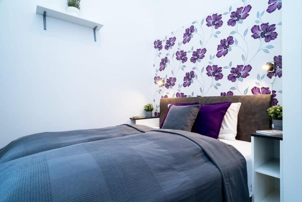 a bedroom with a bed with purple pillows and a floral wall at Modern Intimate Studio in the center in Budapest