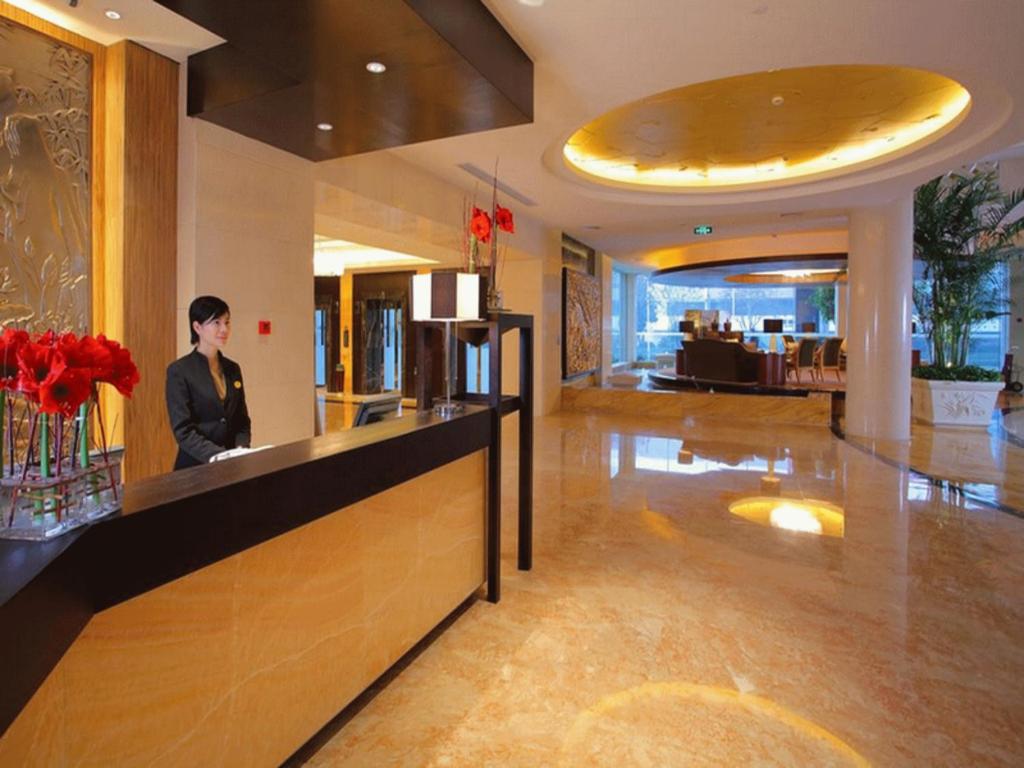 a man standing at a counter in a hotel lobby at New Century Shaoxing Grand Hotel in Shaoxing
