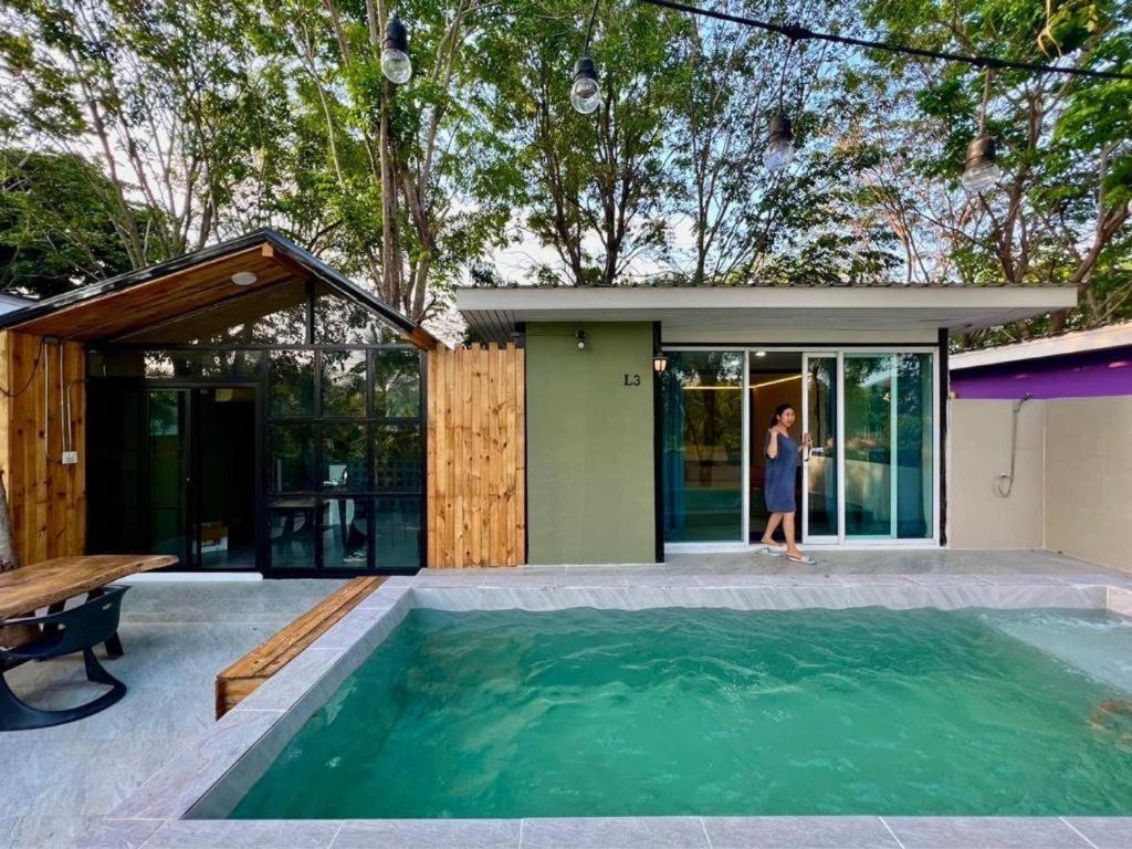 a woman walking in front of a house with a swimming pool at The State Resort in Ban Wat Phrik