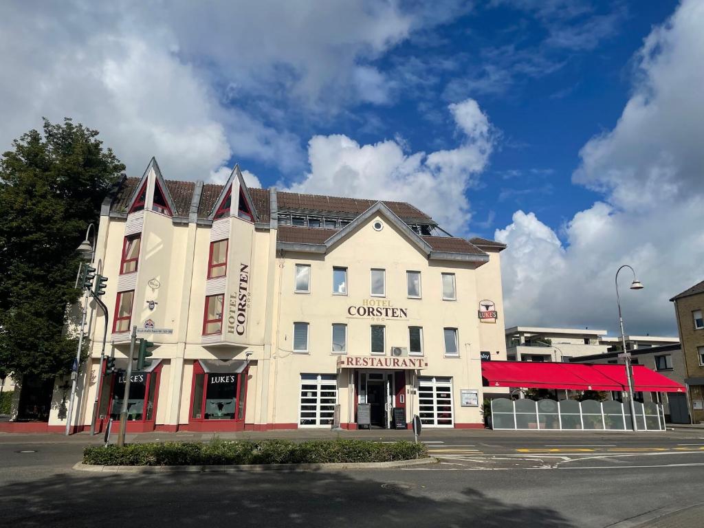 a large white building with a red canopy on a street at Hotel Corsten - Home of Lukes Steaks & More - Heinsberg in Heinsberg