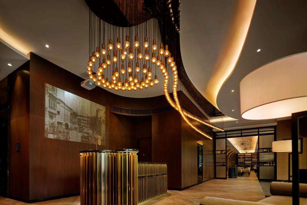 A warmly lit lobby centers on a sculptural ring chandelier and reception desk.