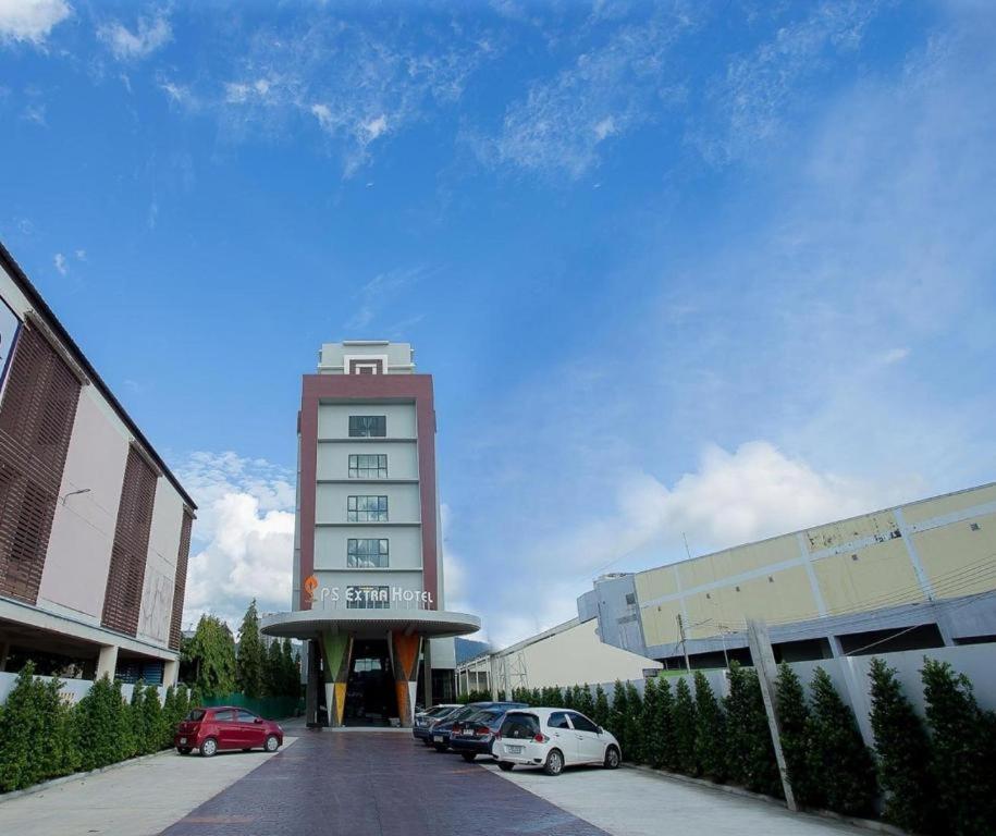 a tall building with cars parked in a parking lot at Ps Extra Hotel in Hat Yai