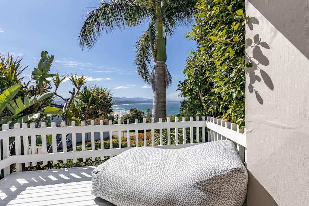 a white bench sitting on a porch with a palm tree at Plett Holiday Stay with Hut Tub ,Pizza Oven and Views in Plettenberg Bay
