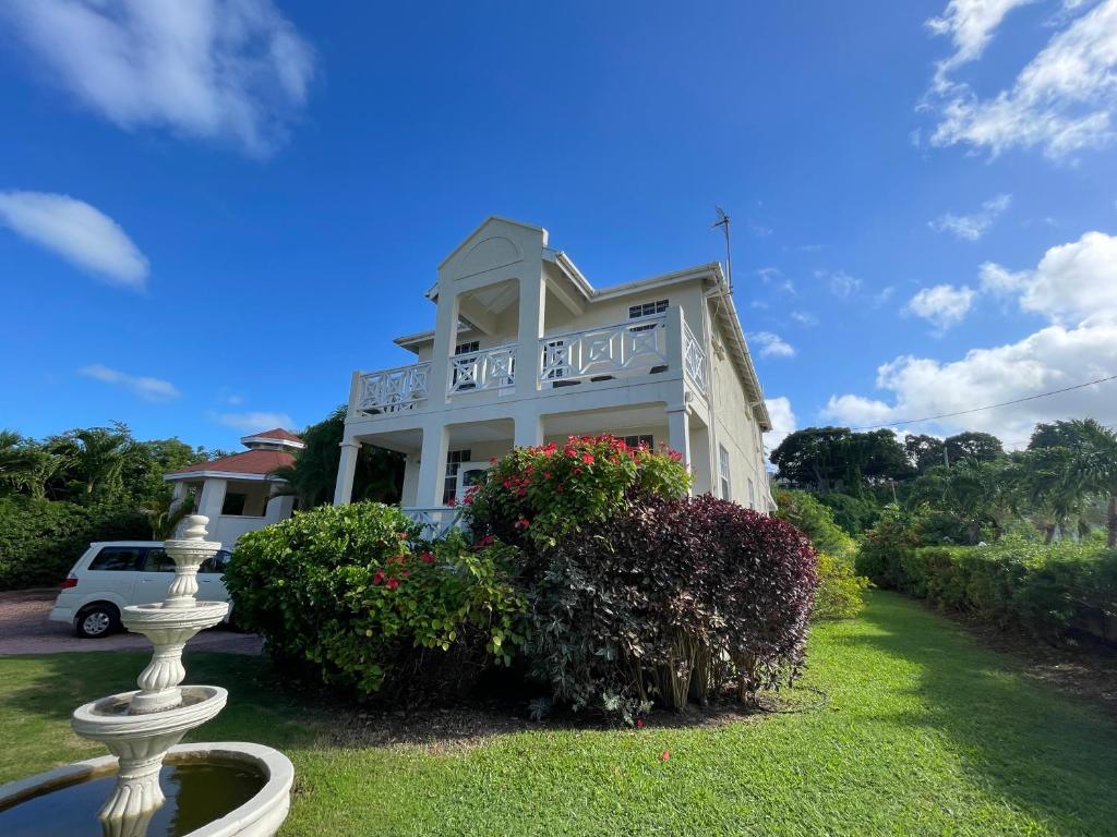 a white house with a porch and bushes at Holland Park Barbados in Saint Peter