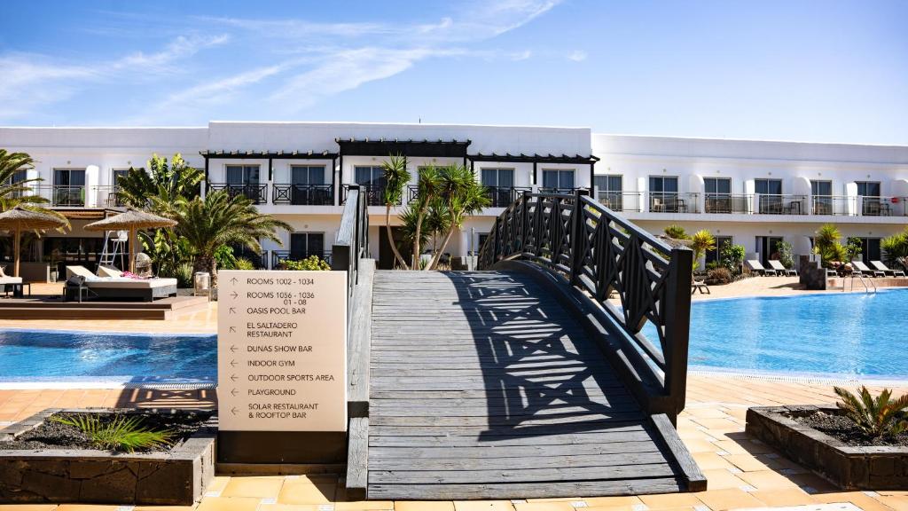 a wooden walkway leading to a resort with a swimming pool at Coral Cotillo Beach in El Cotillo