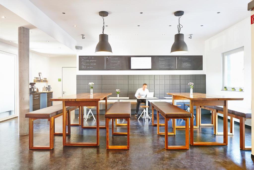 a kitchen with wooden tables and chairs and a person at a2 HOTELS Plochingen in Plochingen