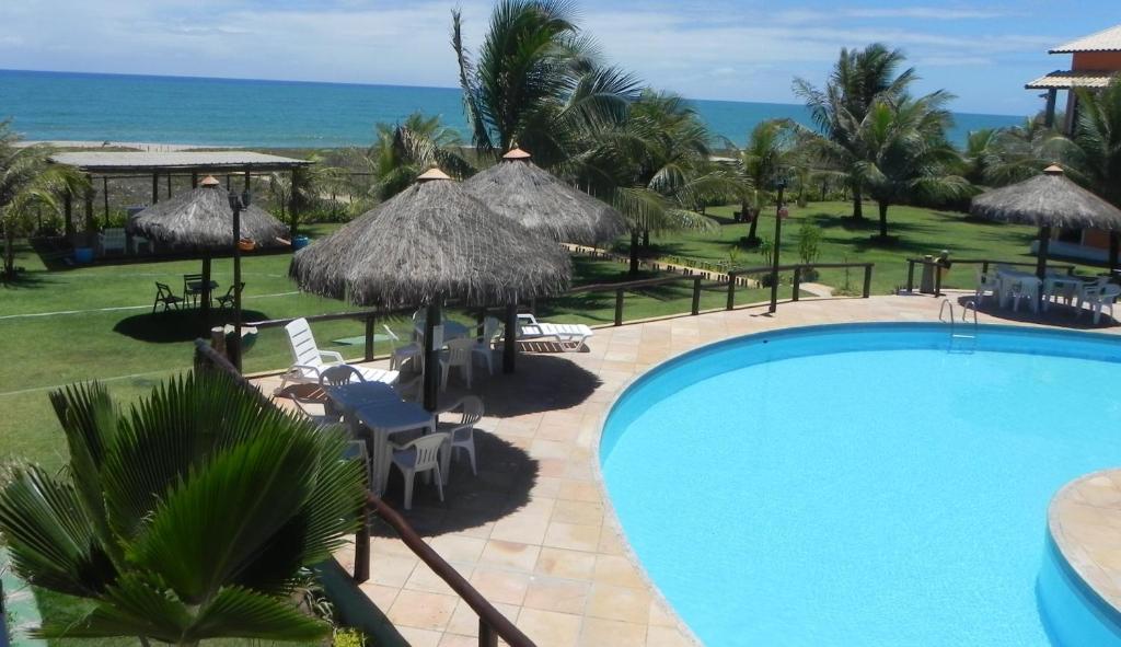 una piscina con sombrillas y sillas y el océano en Village Acapulco - Itacimirim/BA, en Itacimirim