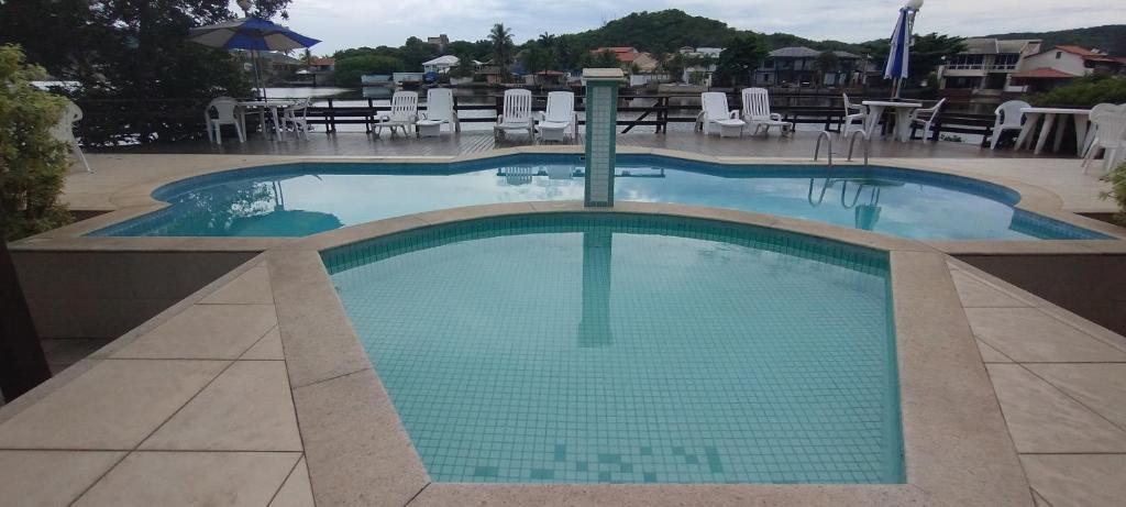 een groot zwembad op een resort met tafels en stoelen bij Casa Duplex com 02 suites completa em Condomínio com Piscina , Sauna , churrasqueiras, deck podendo parar embarcações, próximo as Praias das Conchas e Peró e também linda Ilha do Japônes in Cabo Frio