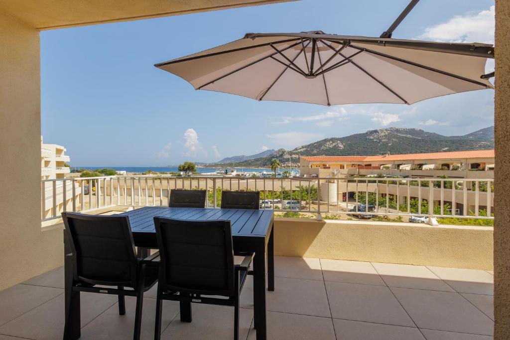 une table et des chaises sur un balcon avec un parasol dans l'établissement Inka - appt vue mer et montagne, à Lumio