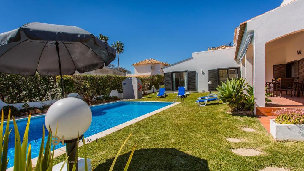 a backyard with a swimming pool and an umbrella at Greice Homes-650 meters from the beach, 4 bedrooms villa for holidays in Vilamoura-Quarteira in Quarteira