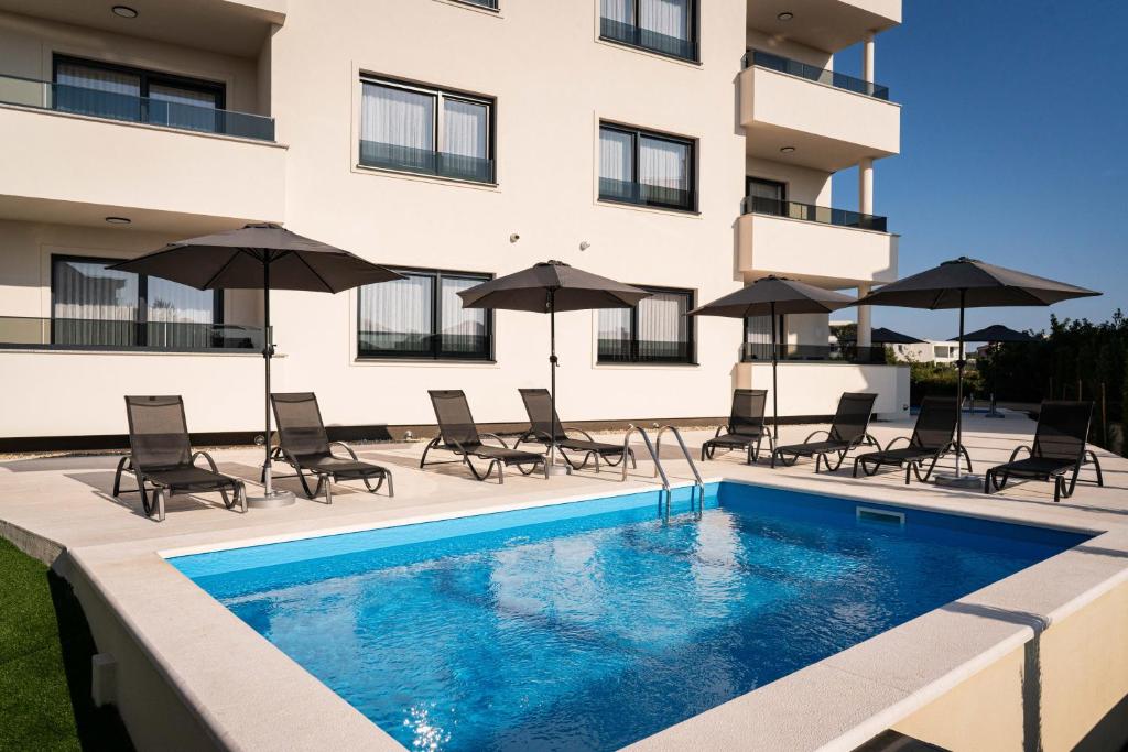 a swimming pool with chairs and umbrellas next to a building at Villa Full Moon Luxury Apartments Novalja in Novalja