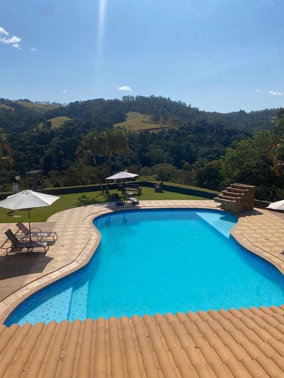 a large blue swimming pool with two tables and umbrellas at Pousada Costa Rielli in Águas de Lindoia