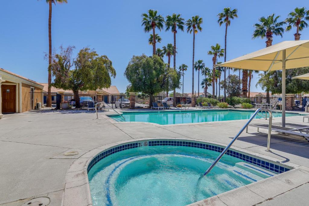 a swimming pool with an umbrella and palm trees at Near Golf Condo with Pool Access in Palm Desert! in Palm Desert