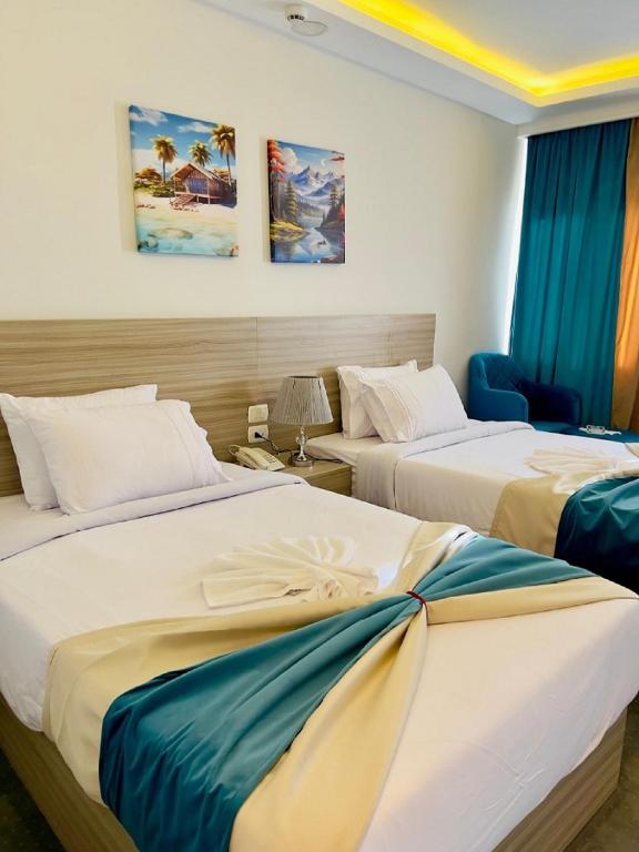two beds in a hotel room with blue curtains at Mar Charbel Hotel Cairo in Cairo