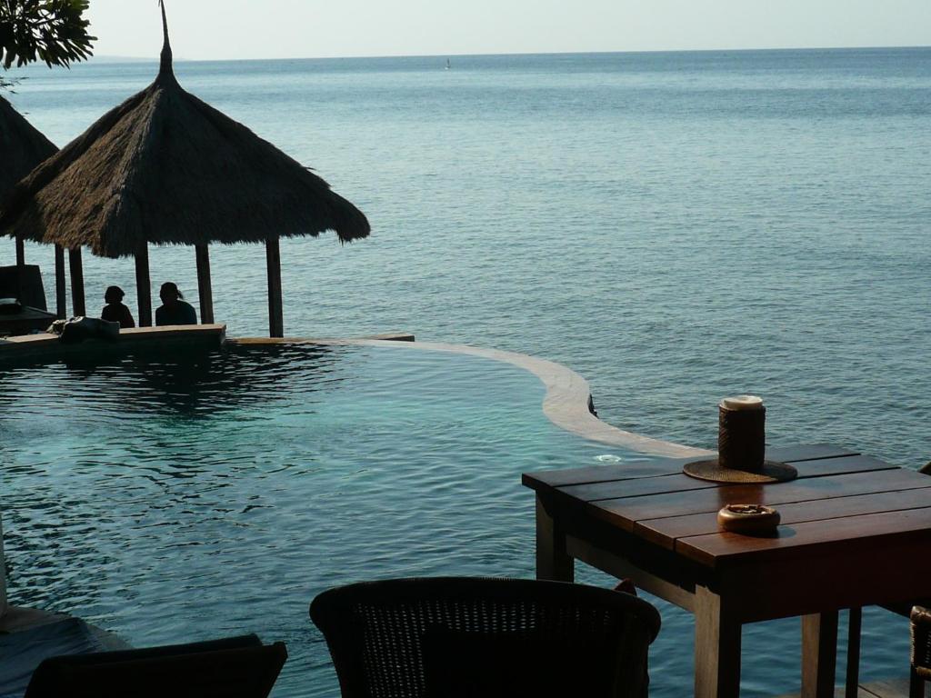 una piscina junto al océano con mesa y sillas en Wawa Wewe II Villas, en Amed