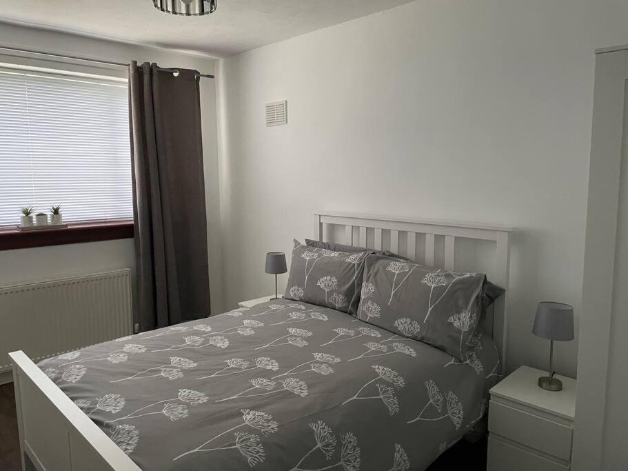 a bedroom with a bed with a gray comforter and a window at 3 bedroom detached house, close to Glasgow in Barrhead