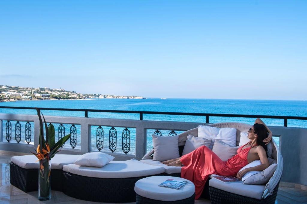 une femme en robe rouge assise sur un canapé sur un balcon dans l'établissement Villa Sonia, à Chersónissos