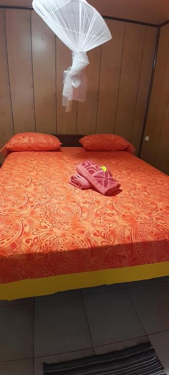a bed with an orange comforter and two pillows at Penu maurua in Te-Fare-Arii