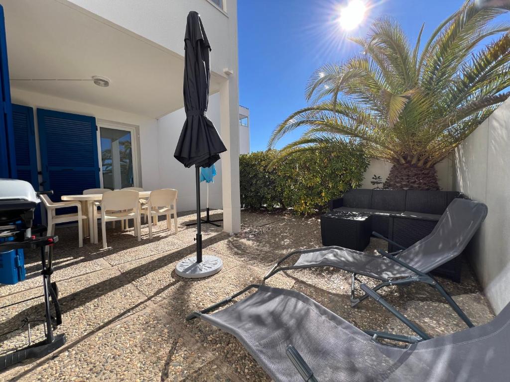 un patio avec un canapé, un parasol et un palmier dans l'établissement Appart RDC T3 proche plage accessible à pieds, au Barcarès