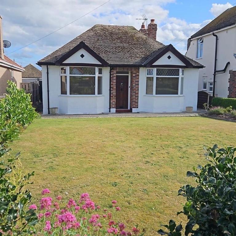 a white house with a yard with pink flowers at Victoria Beach Cottage in Prestatyn
