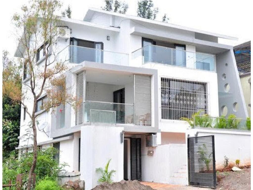 a white house with a balcony in front of it at Triveni Stays Blue Gum 3BHK in Panchgani