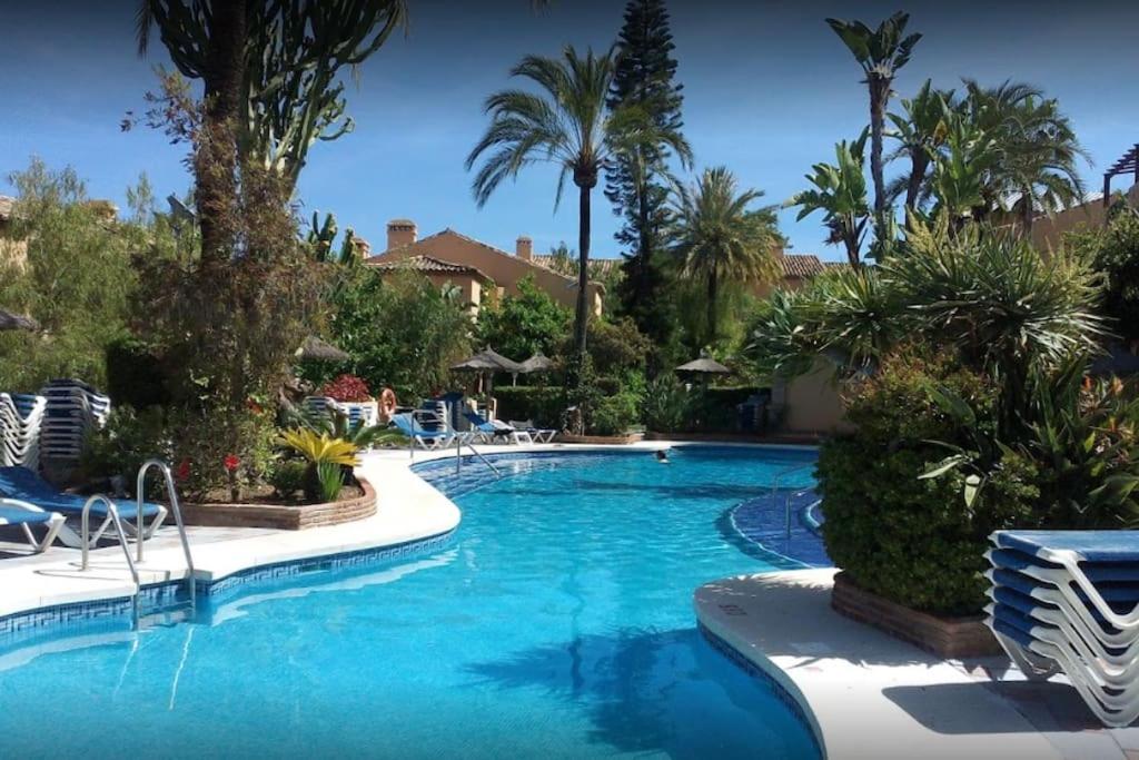 a swimming pool with palm trees and chairs in a resort at Oasis Golf Apartment in Sitio de Calahonda