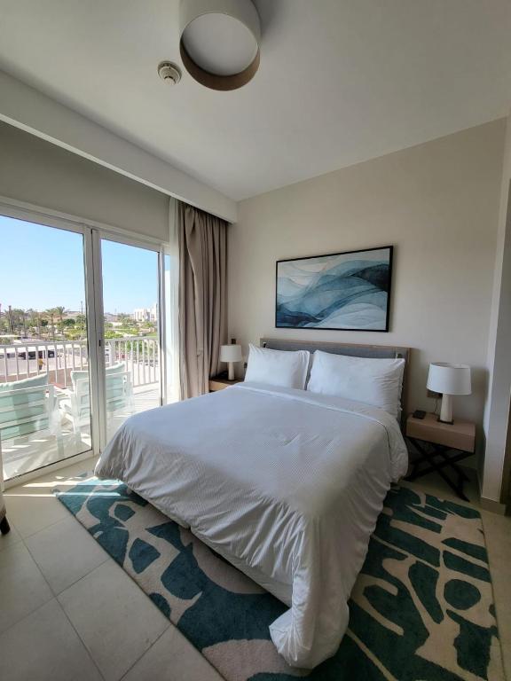 a bedroom with a white bed and a large window at Vida Marina marassi hotel apartment with extra fees for beach or pool access شقة فندقية عائلات فقط في أوتيل فيدا مراسي مارينا دخول شاطئ البحر او حمام السباحة برسوم إضافية in El Alamein
