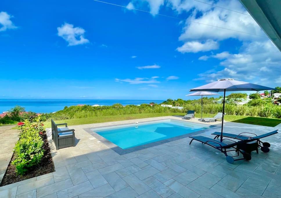 piscina con ombrellone e due sedie e tavolo e ombrellone di Magnifique villa 6 à 8 pers avec piscine - vue mer a Vieux-Habitants