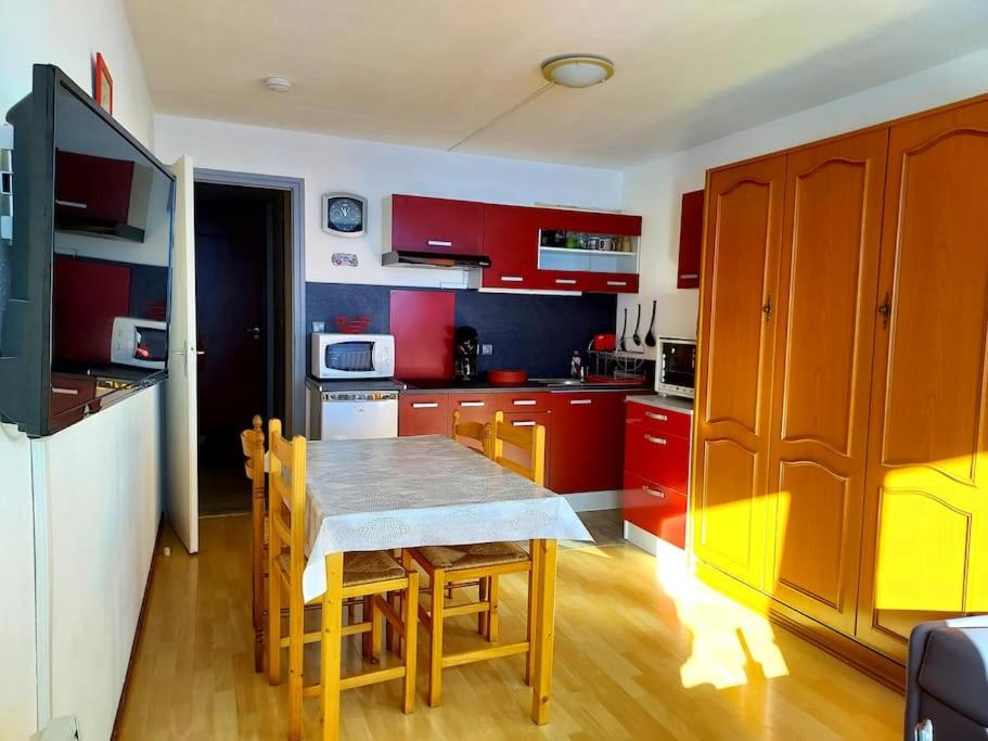 une cuisine avec des placards rouges et une table avec des chaises dans l'établissement Appartement Station de ski La Mongie Pieds des Pistes 6 couchages, à Bagnères-de-Bigorre