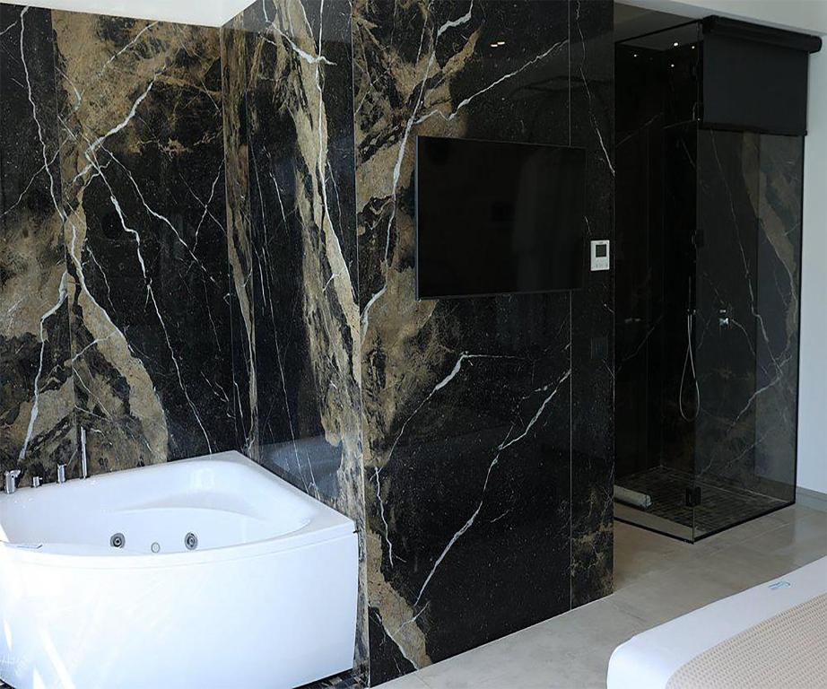 a bathroom with a white tub and a black marble wall at Comfort Suites in Golem