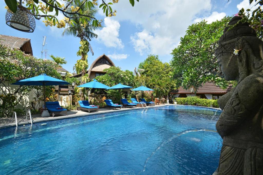 una piscina en un complejo con sillas y sombrillas en Puri Dewa Bharata Hotel & Villas, en Legian