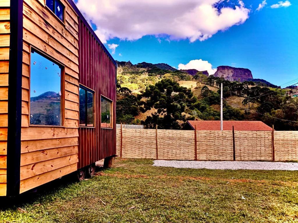une maison en bois avec une clôture et des montagnes en arrière-plan dans l'établissement Tiny House Just Breathe, à São Bento do Sapucaí