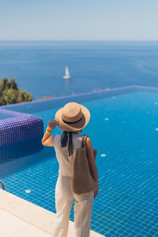 a woman wearing a hat standing next to a swimming pool at La Kumsal Hotel in Kaş
