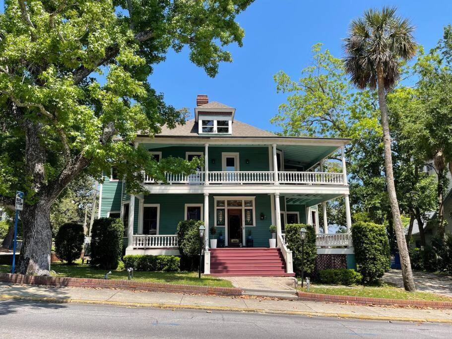 a green house with a white porch and a palm tree at Large Historical Home for Groups Walk to Downtown! in Baptist Hospital Heliport