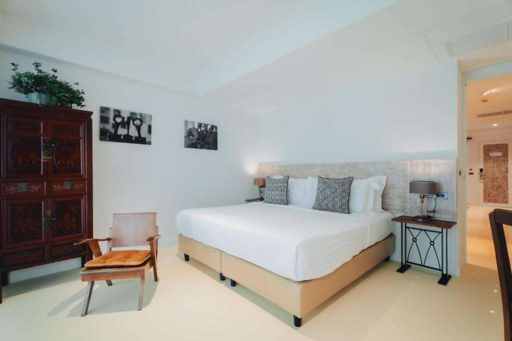 een slaapkamer met een wit bed en een stoel bij Xinlor House - Phuket Old Town in Phuket