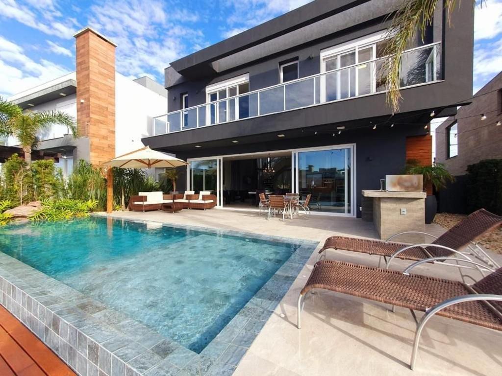 a swimming pool in front of a house at Casa de Verão no Malibu à Beira do Lago in Xangri-lá