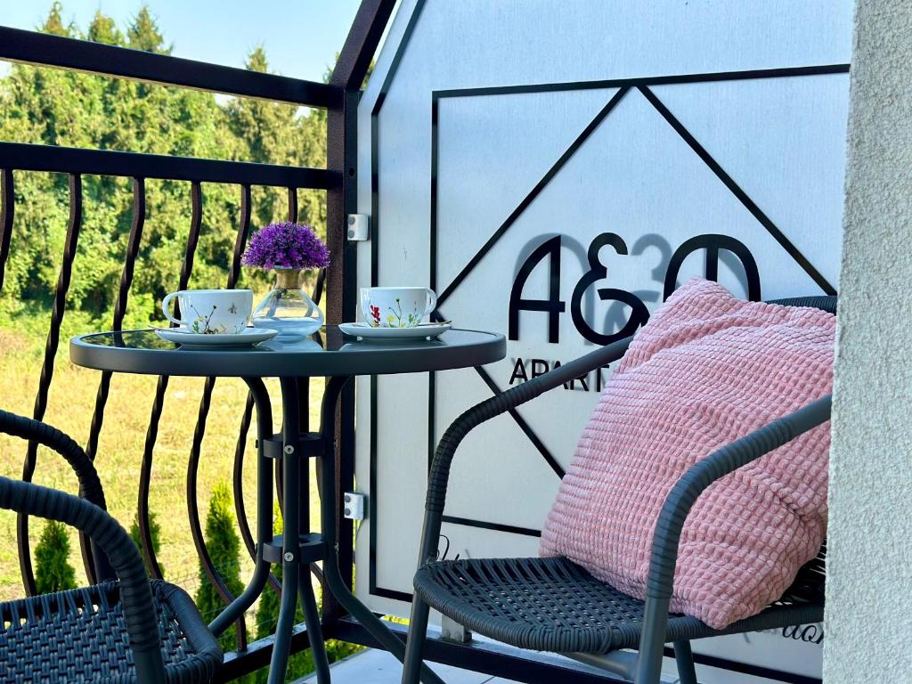 Small balcony bistro set with teacups, purple flowers and a pink cushion beside A&A sign.