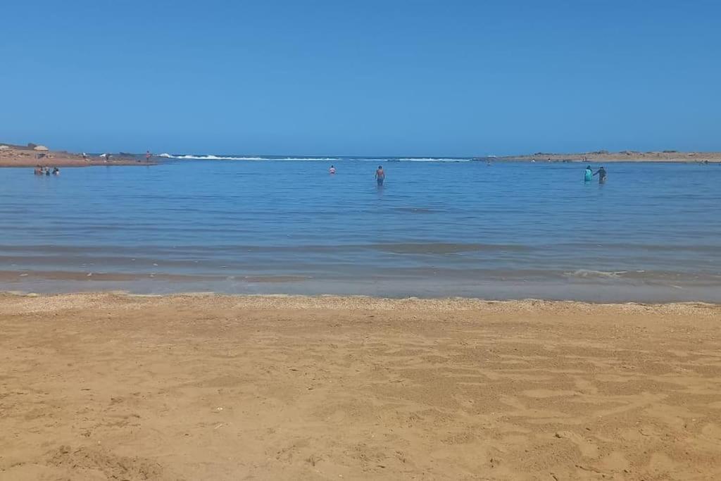 a beach with people swimming in the water at Appart familial près de la plage Val d'or in El Harhoura