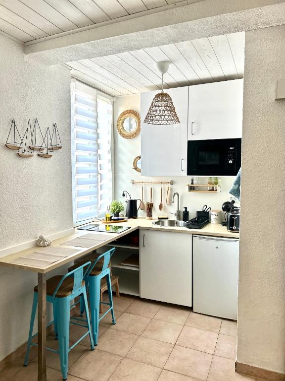 une cuisine avec des placards blancs et une table avec des chaises bleues dans l'établissement Charmant studio au cœur du Mourillon, à Toulon