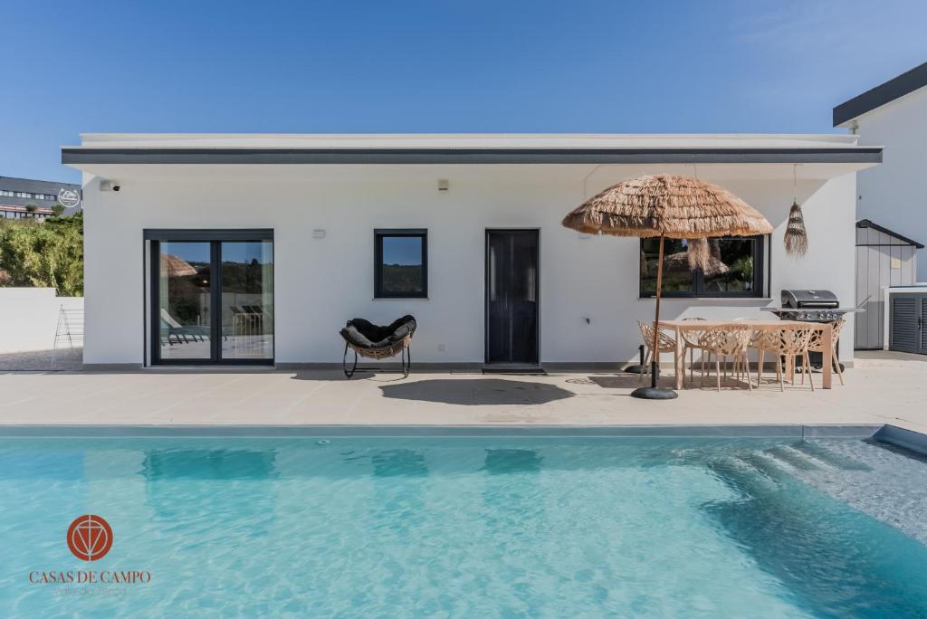 a house with a swimming pool and an umbrella at Casas de Campo - Vale da Terça in Vermelha