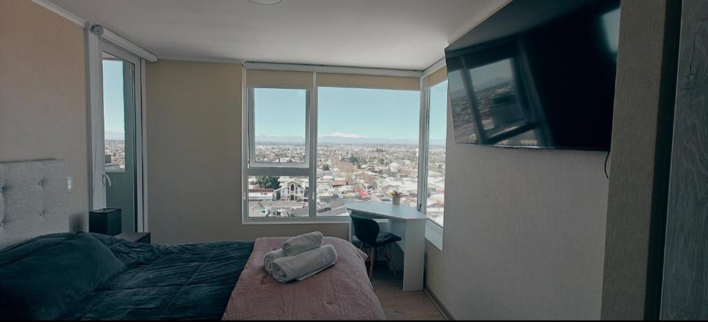a bedroom with a bed and a desk and windows at Depto Cómodo y Equipado en el Centro de Chillan con Estacionamiento in Chillán