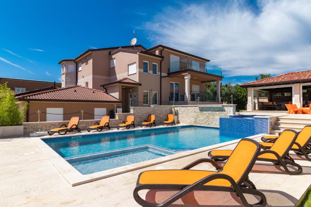 une piscine avec des chaises et une maison dans l'établissement Villa Istra Kamen for kids & families near Pula for 18 people with sport activities, wellness & 67 m2 heated private pool, à Ližnjan