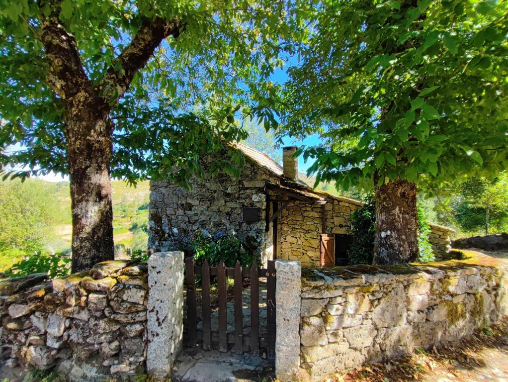 una vieja casa de piedra con una valla y un árbol en Casa da Fonte - Branda da Aveleira, en Melgaço
