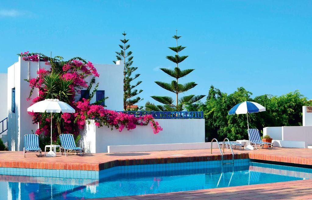 uma piscina com cadeiras, guarda-sóis e flores em Sirius Apartments em Hersonissos