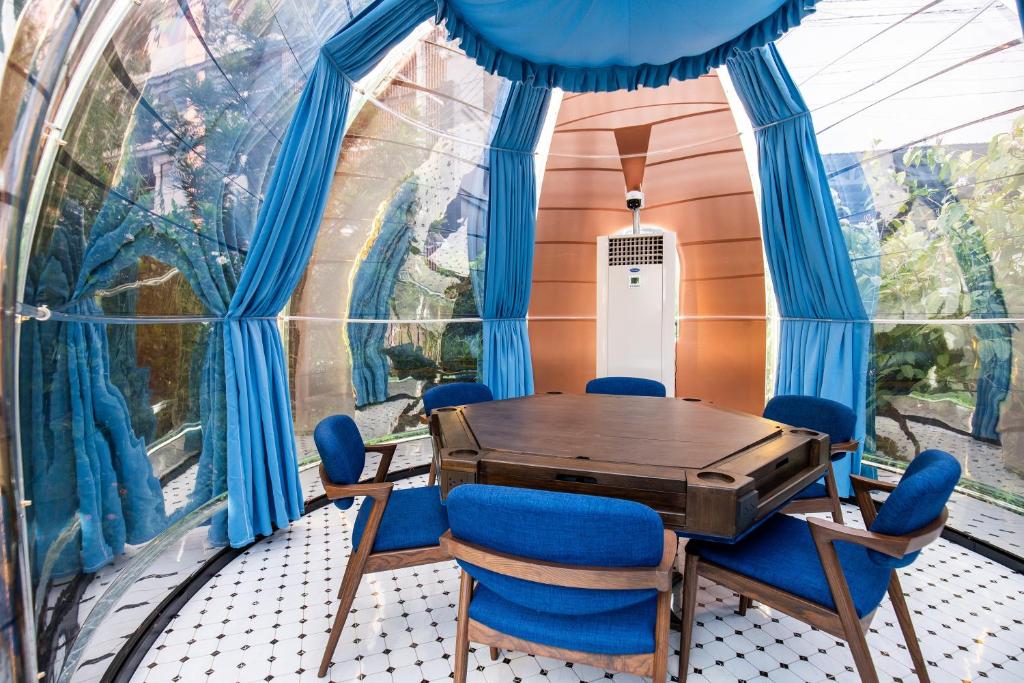 A bright enclosed lounge with a large wooden game table and blue chairs.