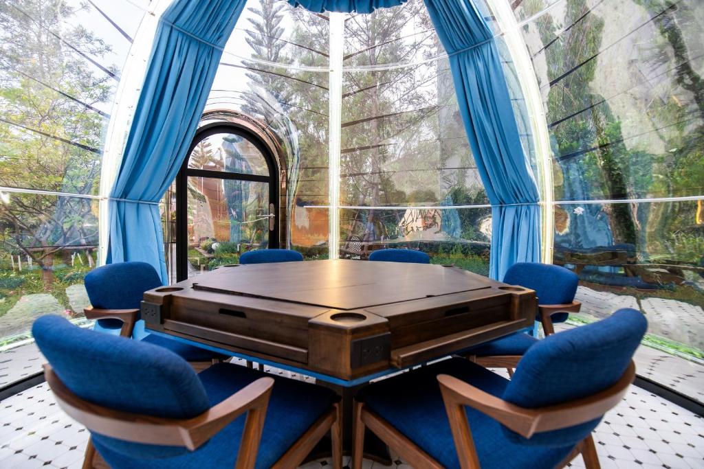 A conference table with blue armchairs fills a glass garden pavilion.